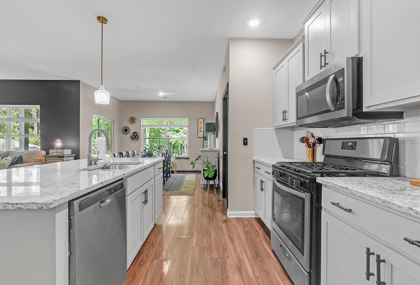 Kitchen featuring stainless steel appliances, light wood finished floors, light stone counters, and an island with sink