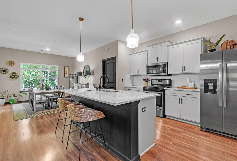 Kitchen featuring stainless steel appliances, a kitchen breakfast bar, pendant lighting, a kitchen island with sink, and gray cabinets