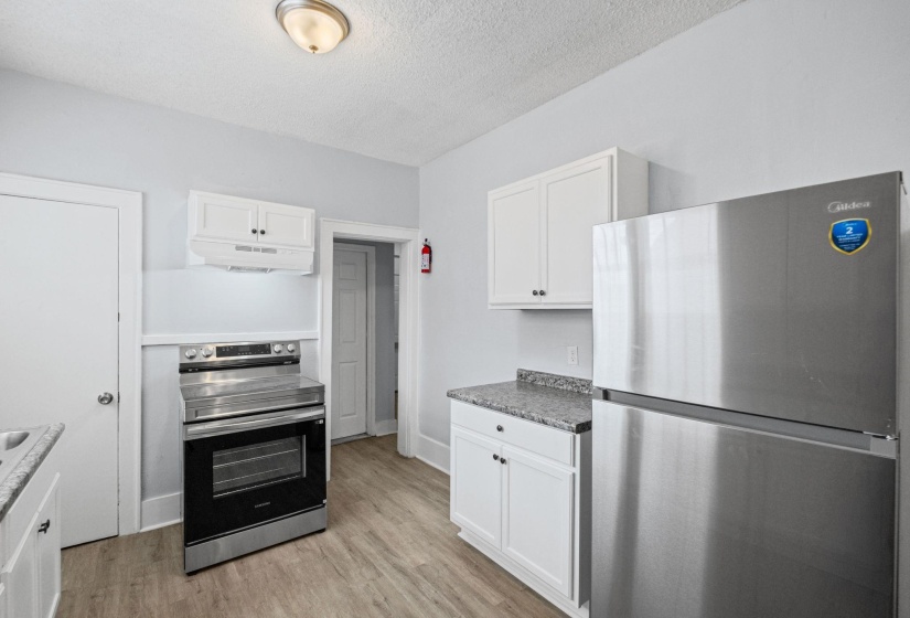 Kitchen with stainless steel appliances, white cabinetry, a textured ceiling, and light wood-type flooring