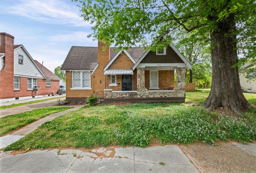 View of front of house with a porch, a front lawn, a chimney, stone siding, and roof with shingles