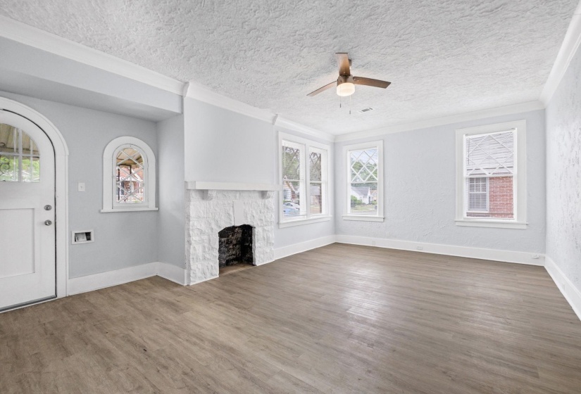 Unfurnished living room featuring ceiling fan, a stone fireplace, dark wood-type flooring, crown molding, and a textured ceiling