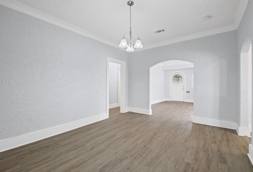 Unfurnished dining area featuring a textured wall, arched walkways, a chandelier, ornamental molding, and dark wood-style floors