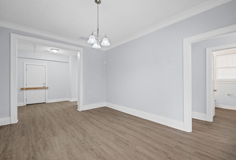 Unfurnished dining area featuring crown molding, wood finished floors, hanging lights, and a textured wall