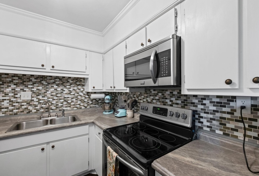 Kitchen with stainless steel appliances, white cabinetry, crown molding, light countertops, and tasteful backsplash