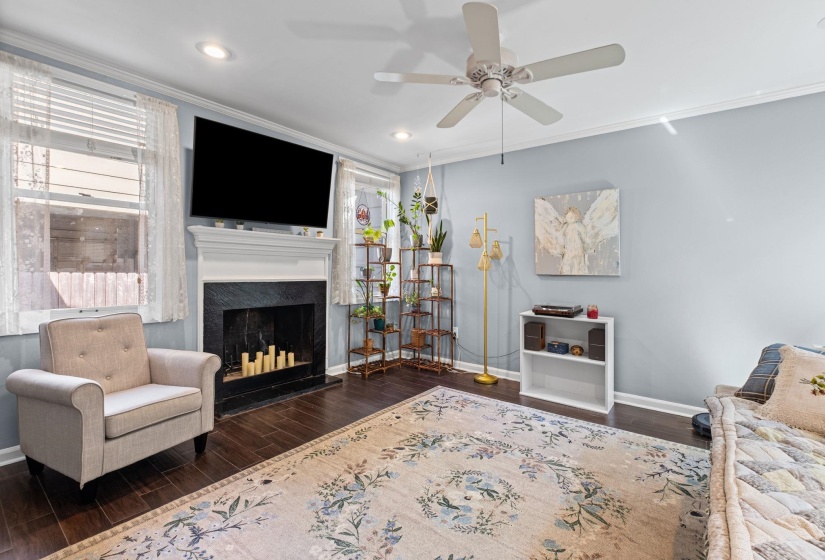 Living room with dark wood-style flooring, ornamental molding, ceiling fan, recessed lighting, and a fireplace with raised hearth