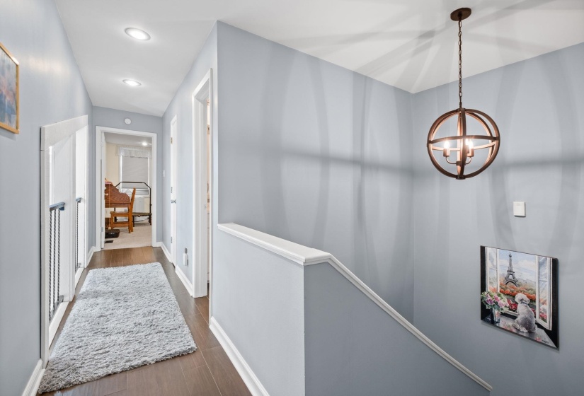 Corridor featuring dark wood-style flooring, hanging lights, and an upstairs landing