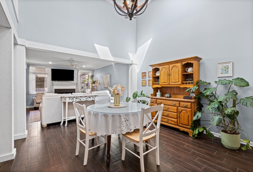 Dining area with wood tiled floors, a ceiling fan, hanging lights, a high ceiling, and a fireplace