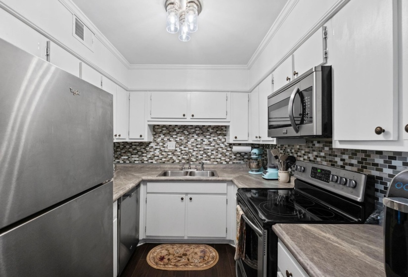 Kitchen featuring stainless steel appliances, white cabinets, crown molding, and light countertops