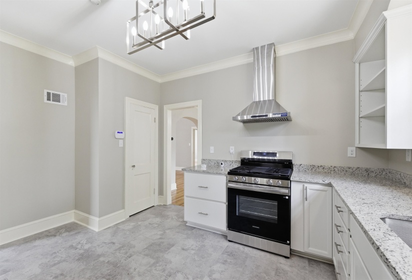 Kitchen featuring stainless steel range with gas cooktop, light stone counters, white cabinets, open shelves, and ornamental molding