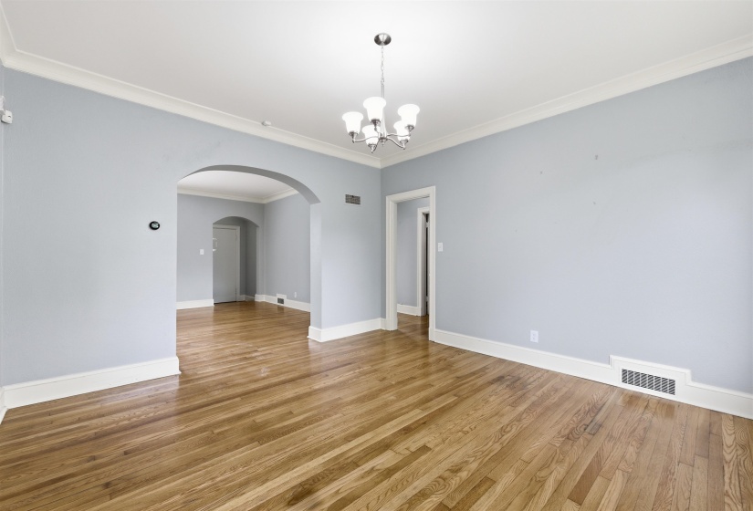 Empty room featuring crown molding, suspended lighting, light wood-style flooring, and arched walkways