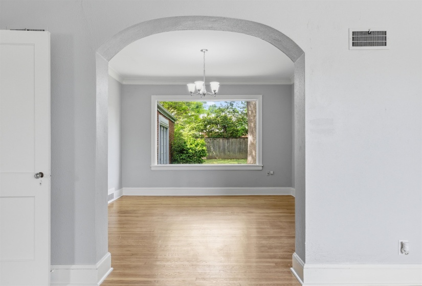 Unfurnished dining area with hanging lights, arched walkways, light wood-style flooring, and ornamental molding
