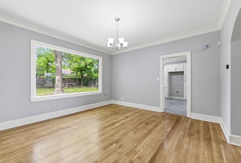 Empty room featuring suspended lighting, light wood-style floors, and ornamental molding