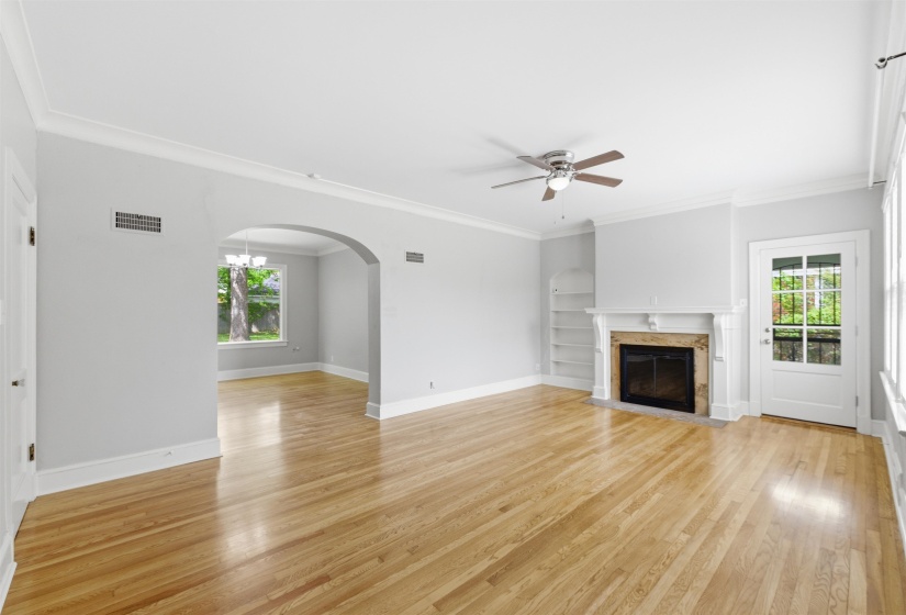 Unfurnished living room featuring ceiling fan, a fireplace with flush hearth, arched walkways, light wood-type flooring, and ornamental molding