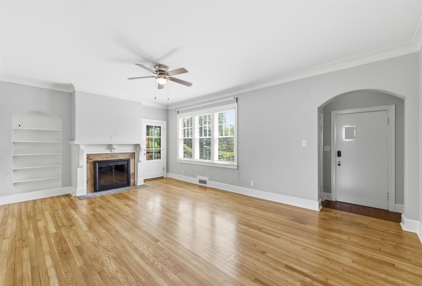 Unfurnished living room with crown molding, arched walkways, a ceiling fan, a high end fireplace, and light wood-style flooring