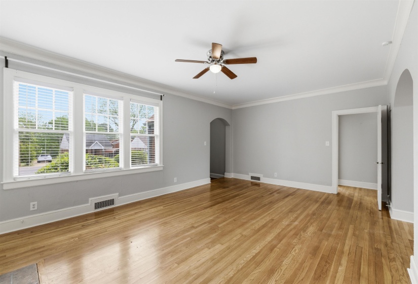 Unfurnished living room featuring arched walkways, light wood-style flooring, ceiling fan, and crown molding