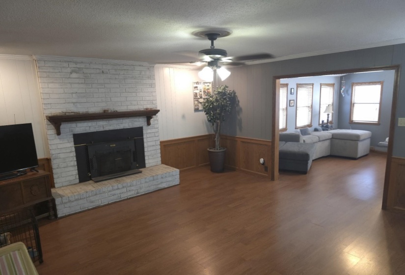 Living room featuring wood walls, ornamental molding, wood finished floors, a ceiling fan, and a fireplace