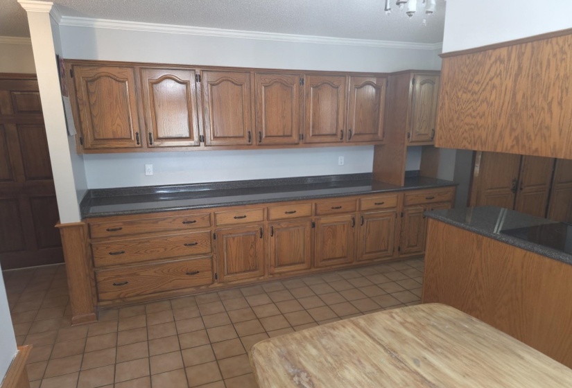 Kitchen with wood finish cabinetry, ornamental molding, light tile patterned floors, range hood, and dark stone countertops