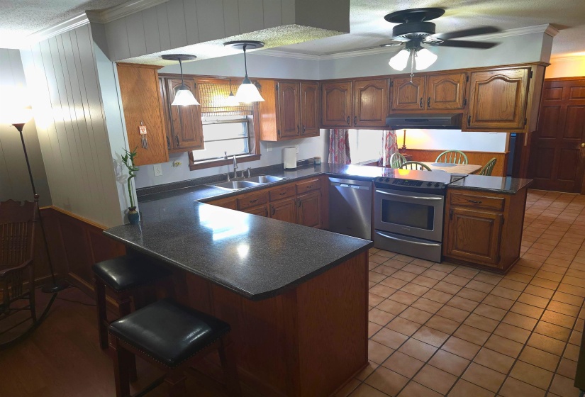 Kitchen featuring a peninsula, crown molding, wood finish cabinetry, dark countertops, and stainless steel appliances