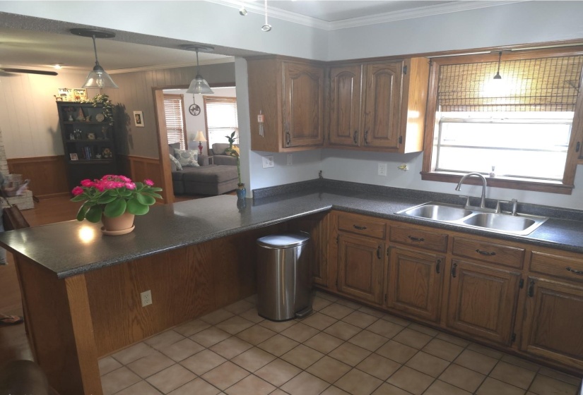 Kitchen with dark countertops, crown molding, a peninsula, decorative light fixtures, and wood finish cabinetry