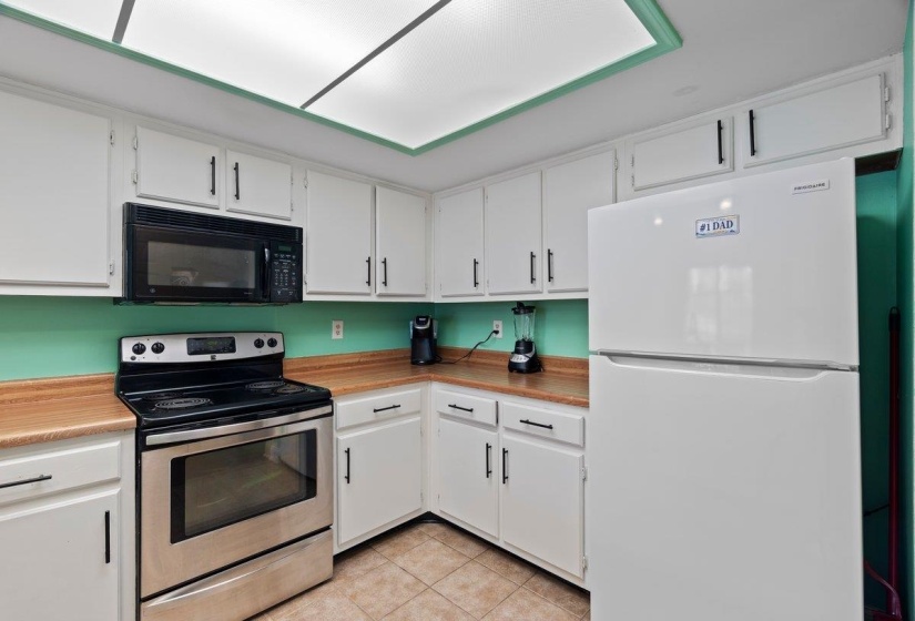 Kitchen with freestanding refrigerator, stainless steel electric range, and white cabinets