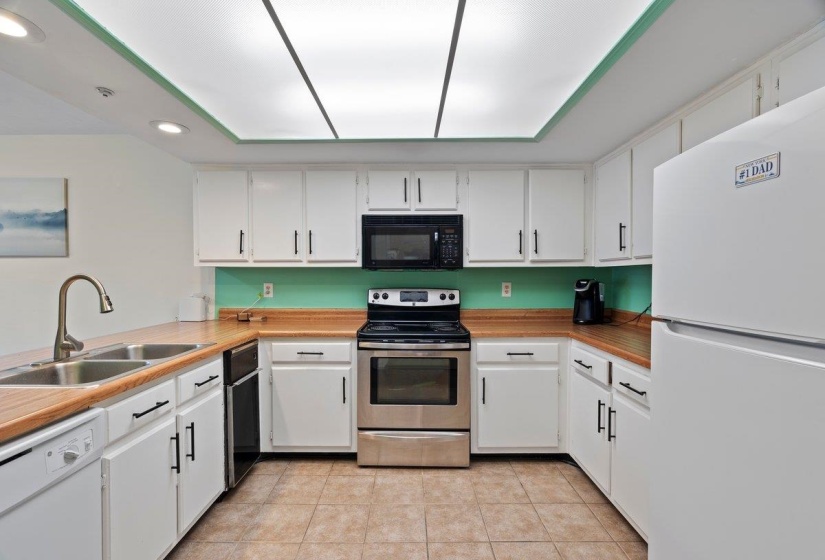 Kitchen with white appliances, white cabinets, light countertops, light tile patterned floors, and recessed lighting