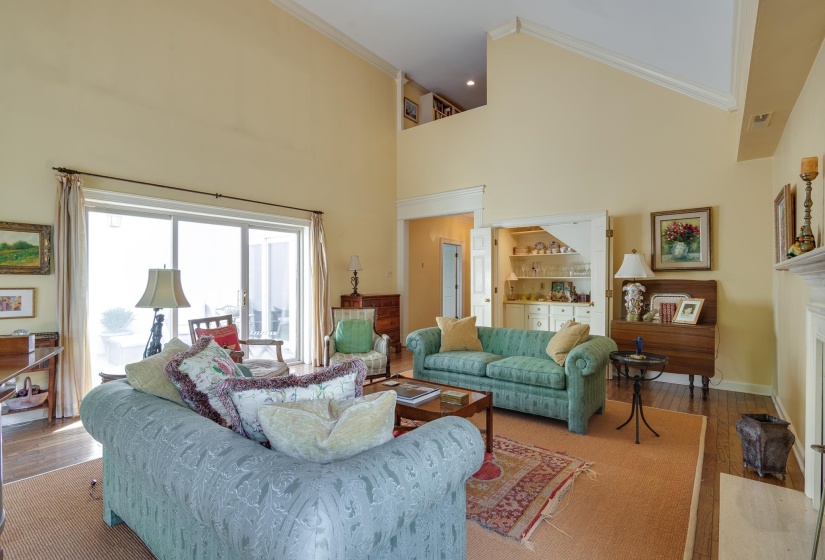 Living room featuring crown molding, wood-type flooring, a fireplace with flush hearth, a high ceiling, and recessed lighting