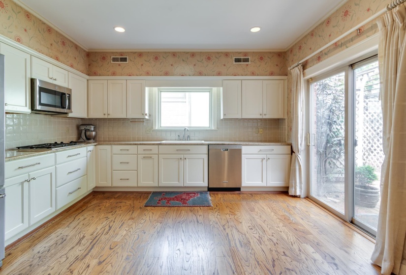 Kitchen with white cabinetry, wallpapered walls, stainless steel appliances, light wood-type flooring, and decorative backsplash