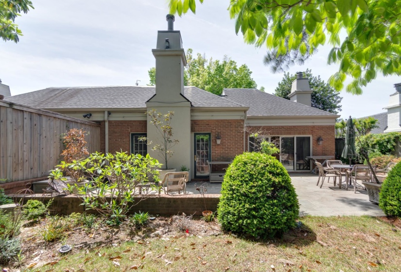 Back of house featuring a chimney, a patio, brick siding, and a shingled roof
