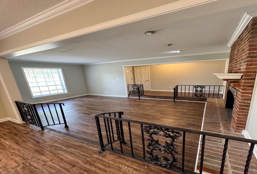Unfurnished living room with a textured ceiling, crown molding, dark wood finished floors, and a brick fireplace