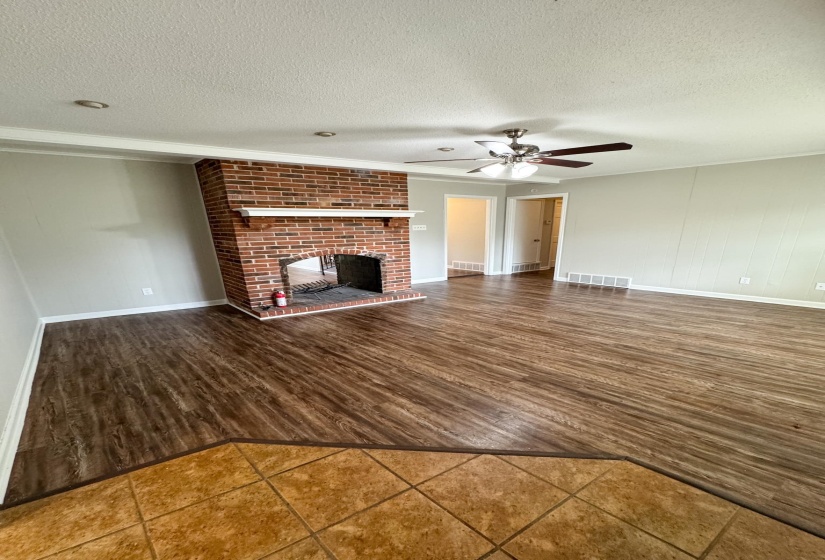 Unfurnished living room featuring dark wood-style flooring, a fireplace, a ceiling fan, and a textured ceiling