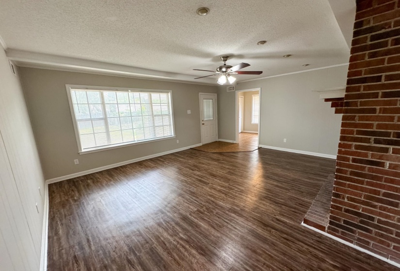 Unfurnished living room featuring dark wood-type flooring, a textured ceiling, plenty of natural light, a ceiling fan, and ornamental molding
