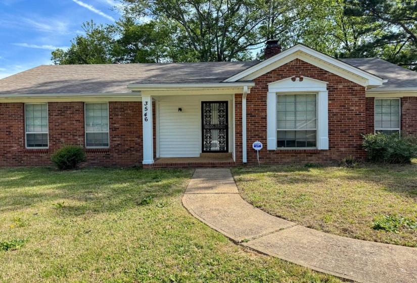 Single story home featuring a porch, brick siding, a chimney, and a front yard