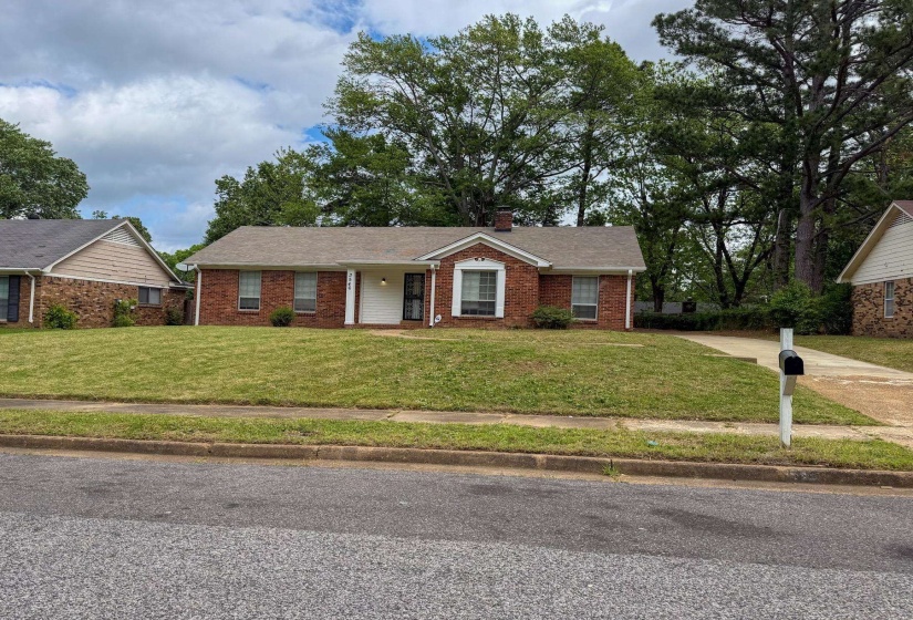 Ranch-style home with a front lawn, brick siding, a chimney, a shingled roof, and a porch