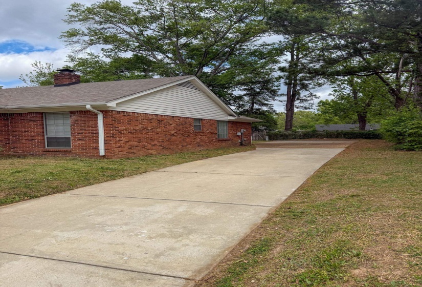 View of side of home with brick siding, driveway, a chimney, and a lawn