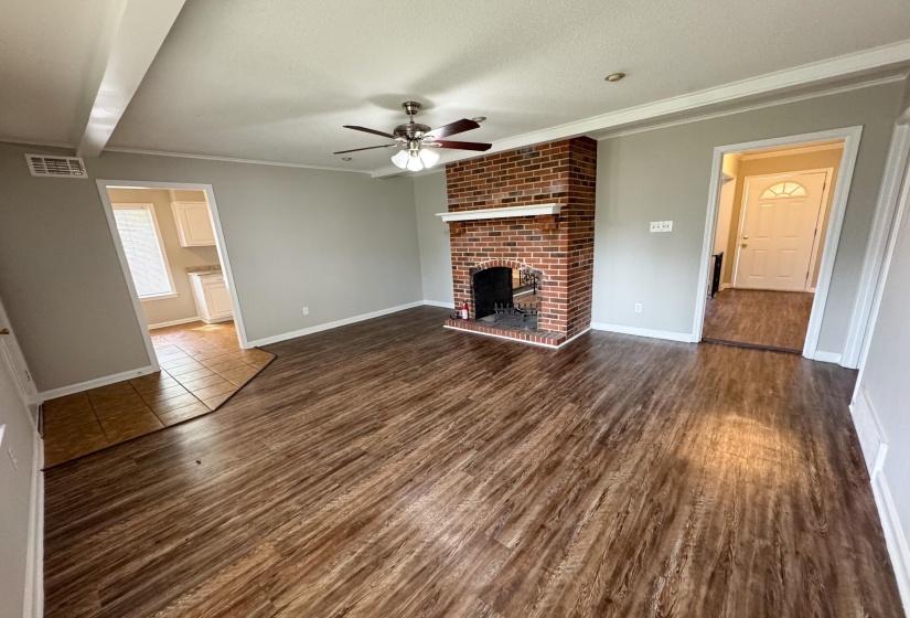 Unfurnished living room with a ceiling fan, a textured ceiling, ornamental molding, dark wood-type flooring, and a brick fireplace