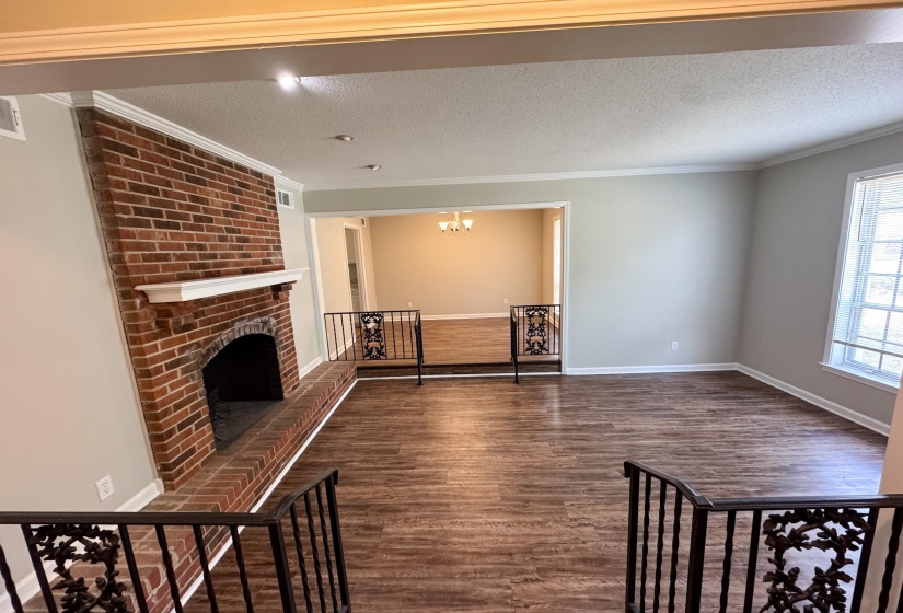 Unfurnished living room with dark wood-style floors, a fireplace, a textured ceiling, hanging lights, and crown molding