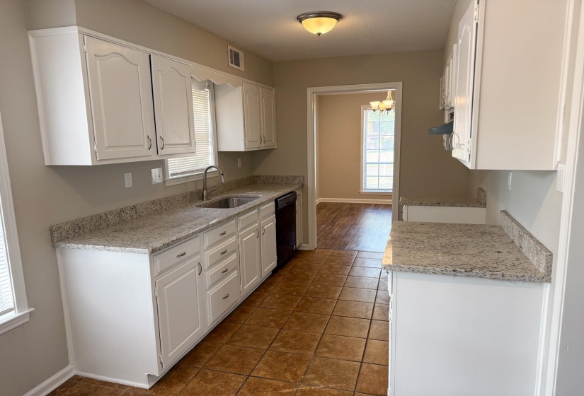Kitchen featuring white cabinets, light stone countertops, dark tile patterned flooring, black dishwasher, and hanging lights