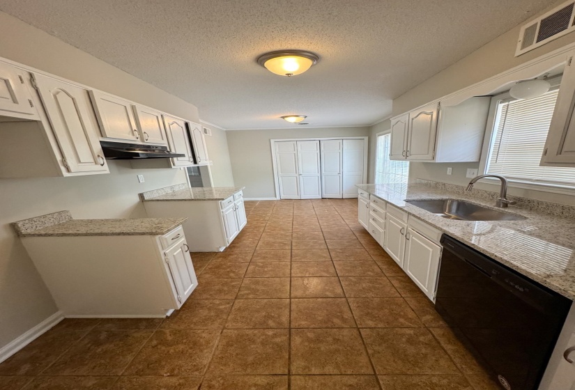 Kitchen featuring black dishwasher, white cabinetry, a textured ceiling, light stone counters, and dark tile patterned floors