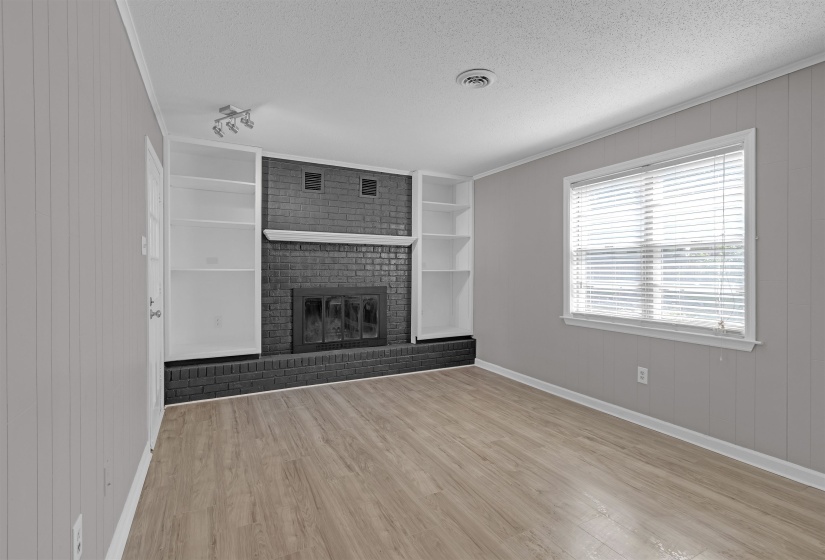 Unfurnished living room featuring wooden walls, a textured ceiling, light wood finished floors, crown molding, and a brick fireplace