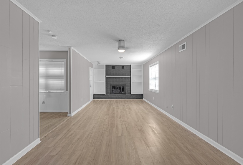 Unfurnished living room with a textured ceiling, built in shelves, light wood-style flooring, a brick fireplace, and wooden walls