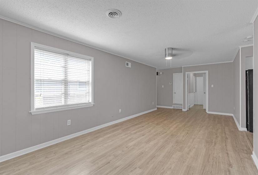 Unfurnished room with light wood-style flooring, a ceiling fan, a textured ceiling, ornamental molding, and wood walls