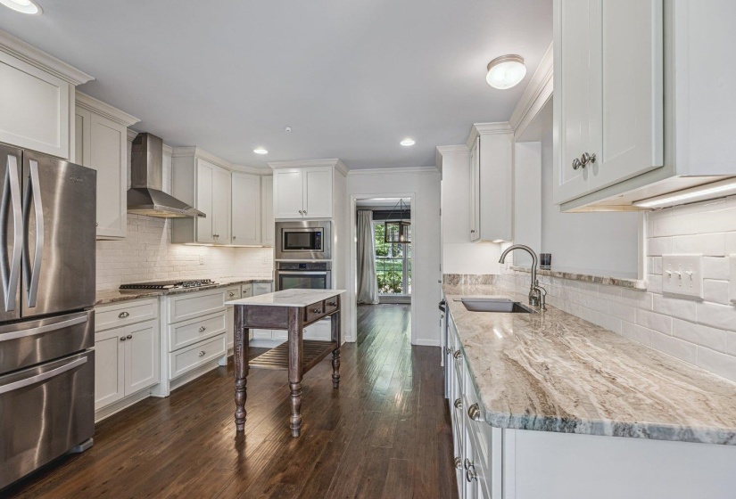 Kitchen with stainless steel appliances, light stone counters, dark wood-type flooring, white cabinetry, and crown molding