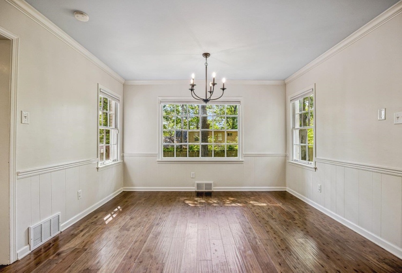 Unfurnished dining area with suspended lighting, wainscoting, dark wood finished floors, ornamental molding, and wood walls