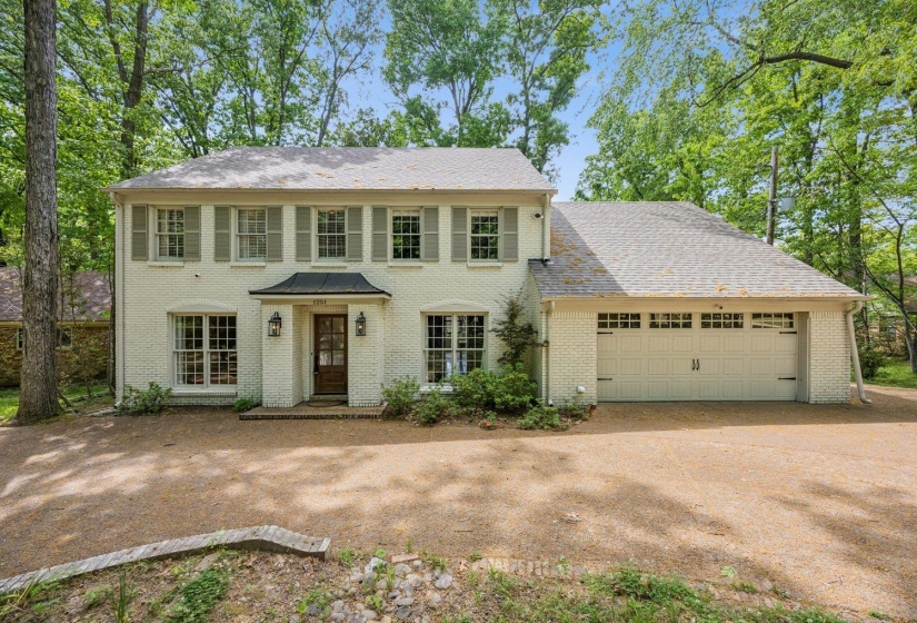 Colonial home featuring a garage, dirt driveway, and brick siding