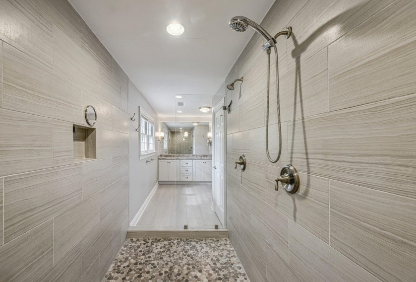 Bathroom featuring double vanity, tile walls, tiled shower, and light tile patterned flooring