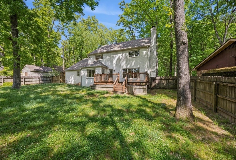 Rear view of property featuring a wooden deck, a chimney, a fenced backyard, stucco siding, and view of scattered trees
