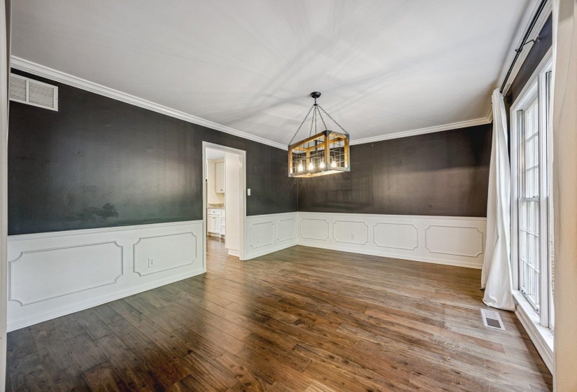 Unfurnished dining area featuring wainscoting, a decorative wall, dark wood finished floors, hanging lights, and crown molding