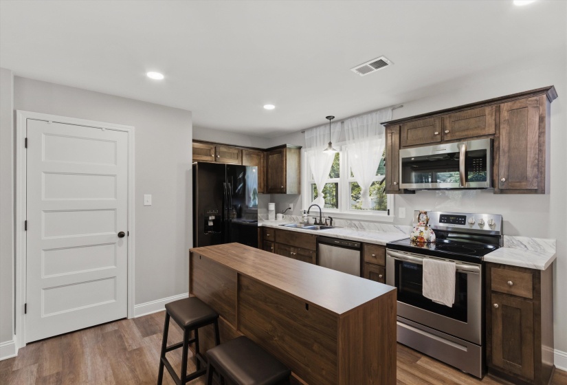 Kitchen with stainless steel appliances, dark wood finish cabinetry, a breakfast bar area, pendant lighting, and dark wood-style floors