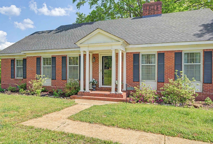 View of front of property featuring brick siding, a chimney, roof with shingles, and a front lawn