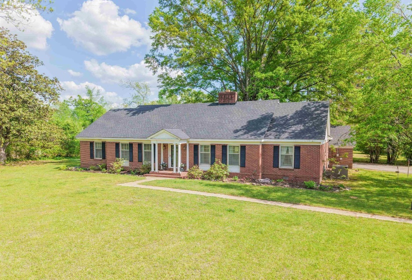 View of front of property featuring a front lawn, brick siding, a chimney, roof with shingles, and a porch